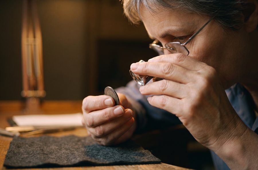 A coin held in one hand under a loupe, over a felt cloth.